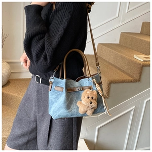 Detail of light blue denim bucket bag with plush puppy charm and brown leather straps