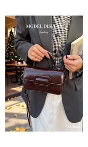 Detail of glossy deep coffee faux leather handbag featuring a large decorative buckle