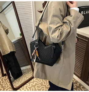 Détail du sac seau plissé noir avec breloque en bois porté avec un trench-coat beige