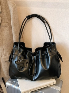 Chic black drawstring bucket bag with star pendant on a metallic travel suitcase