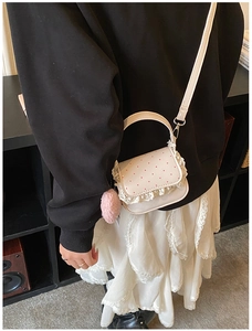 Détail de la dentelle, des pois et du pompon rose sur le sac à bandoulière crème
