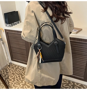 Détail du sac seau plissé noir avec ouverture en V et breloque à pompon en perles ethniques