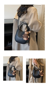 Detail of black lychee grain bucket bag featuring a cute teddy bear plush charm