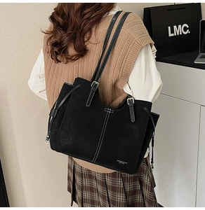 Detail of a black matte leather tote bag with white stitching and drawstring on a model