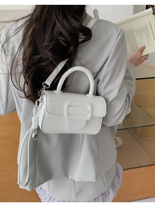 Detail of white leather handbag featuring a silver square buckle and elegant fringe tassel