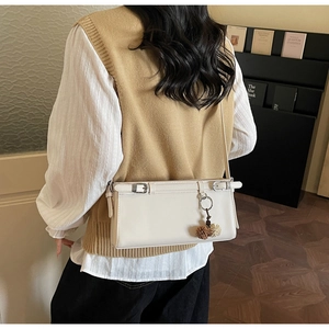 Chic beige shoulder bag with silver buckle and brown plush charm on a model