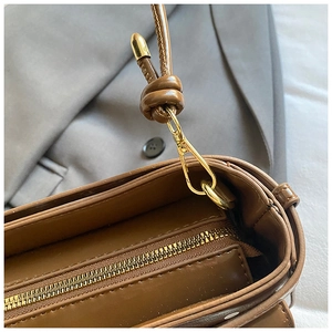 Détail d'un sac en cuir marron avec fermeture éclair dorée et nœud décoratif sur la bandoulière