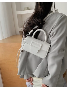 Detail view of white leather crossbody bag with a square buckle on a grey blazer outfit