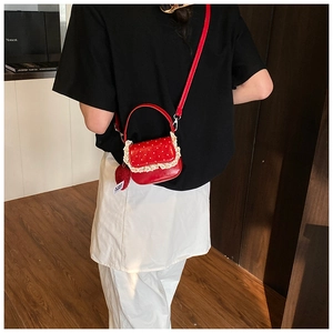 Détail d'un mini sac rouge à pois avec bordure en dentelle et pendentif pompon