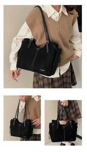 Detailed close-up of a black tote bag with white contrast stitching and shoulder straps
