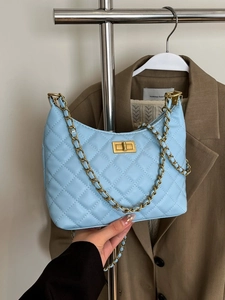 Sac à bandoulière matelassé bleu clair avec chaîne dorée présenté dans une scène de mode