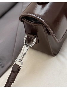 Macro shot of silver hardware and stitching on dark brown glossy leather handbag