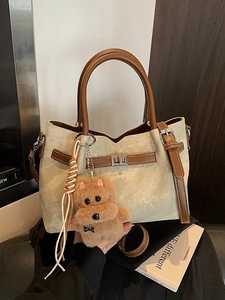 Minimalist beige textured bucket bag with brown leather handles and a plush dog charm