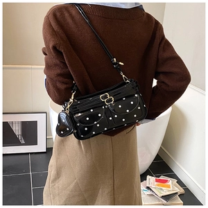 Gros plan d'un sac à bandoulière noir verni à pois avec petit accessoire en forme de cœur