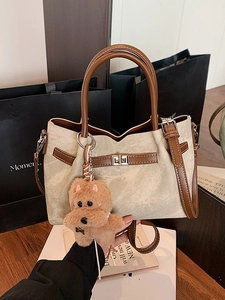 Elegant beige bucket bag with brown leather handles and a plush puppy pendant