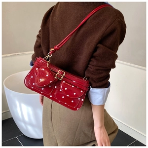 Sac bandoulière rouge à pois avec pendentif cœur et deux poches avant porté par mannequin