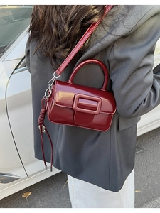 Detail of burgundy glossy patent leather handbag showing crossbody strap and handle