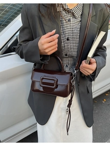 Detail of deep brown glossy leather handbag with oversized buckle and adjustable strap