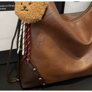 Detail of retro brown faux leather shoulder bag featuring metal rivets and a cute bear charm