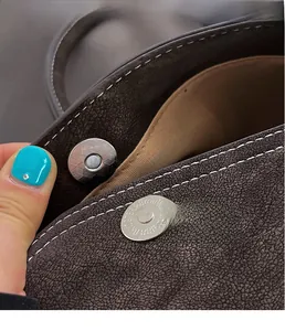 Macro shot of the magnetic hardware clasp on a brown textured leather handbag with stitching