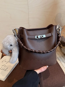 Sac seau en cuir marron avec anse tressée et breloque lapin en peluche sur fond en bois