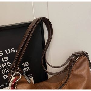 Detail of brown PU leather bag showing silver zipper, metal ring and woven decorative strap