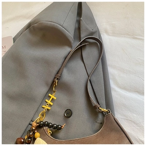 Détail d'un sac vintage en cuir marron avec pendentif H doré et perles sur veste grise