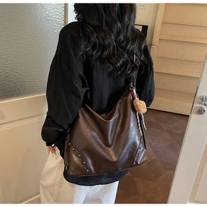 Detail view of large dark brown leather hobo bag featuring rivet trim and a plush bear charm