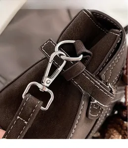Close-up of dark brown leather handbag with white stitching and silver metal hook detail