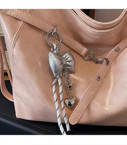 Detail of a silver metallic bow and heart charm on a peach textured leather bag