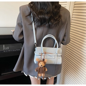 Detail of light blue crossbody bag with brown bear charm shown on person for size scale