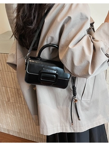 Detailed view of a black leather handbag with a large square buckle worn by a model