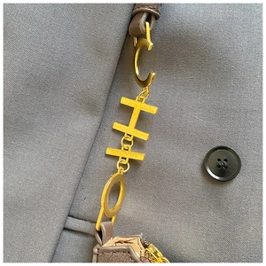 Détail de la chaîne dorée avec lettres C-H-O et bandoulière en cuir marron du sac à épaule