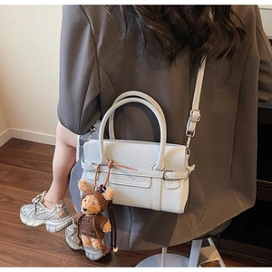 Close-up of matte beige leather handbag featuring a brown teddy bear charm and twin handles