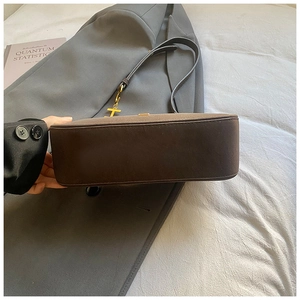 Détail d'un sac à bandoulière en daim marron foncé montrant la base et le pendentif T
