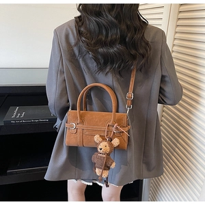 Detail of a brown suede handbag featuring a plush bear charm and sleek silver hardware