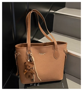 Brown leather tote bag featuring a cute teddy bear pendant and branded typography details