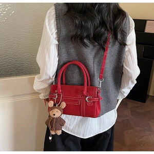 Red crossbody bag with contrast stitching and bear charm shown on a stylish model