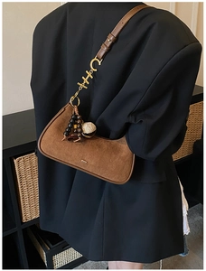 Détail du sac croissant en daim marron avec lettres dorées et pompon en perles