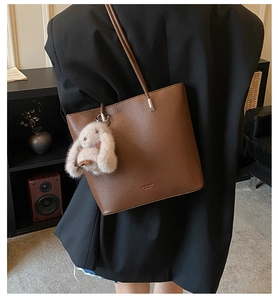 Detailed back view of a brown leather bucket bag with a plush bunny charm on a model
