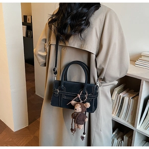 Detail of a black matte leather handbag with white stitching and a cute bear charm