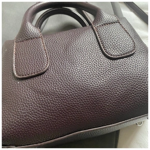 Detail of burgundy pebbled leather handbag featuring sturdy handles and metal bottom studs