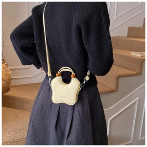 Detail of cream crossbody bag featuring wavy edges and decorative brown wooden beads