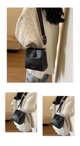 Detail of black bucket bag with wide jacquard strap and litchi texture finish
