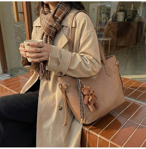 Brown tote bag with cute bear charm and tassel detail shown in a street style setting