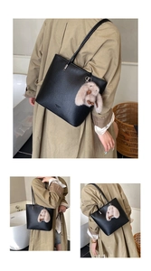 Detail of black pebbled leather tote bag with a plush bunny charm on a model