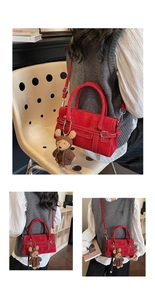 Detail view of red leather handbag with white stitching, buckle and cute bear charm