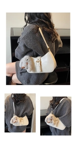 Close-up of a white crescent shoulder bag with leather belt buckle and plush bunny charm