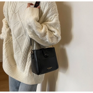 Detail of black textured leather bucket bag with wide strap on a knit sweater