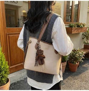 Detail of canvas tote bag with brown leather trim and a cute plush bear charm accessory